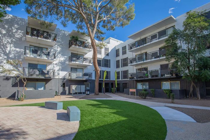 Modern apartment building exterior with spacious balconies and lush landscaping under a clear blue sky.