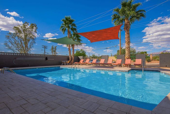 Inviting outdoor pool area with palm trees, colorful shade sails, and comfortable lounge chairs under a clear blue sky.