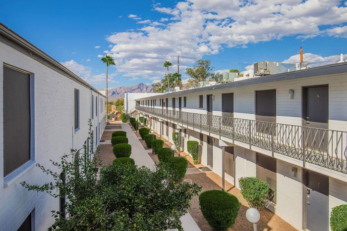 Charming apartment complex with a well-maintained walkway, lush greenery, and picturesque mountain views under a vibrant blue sky.