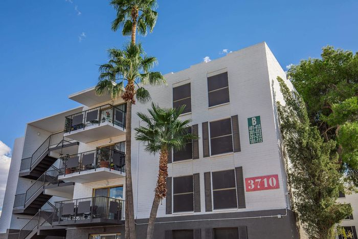 Modern apartment building with stylish balconies and lush palm trees set against a bright blue sky.