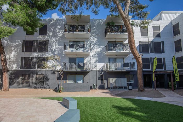 Charming apartment exterior with modern balconies, surrounded by lush greenery and bright blue skies. Inviting and spacious outdoor area perfect for relaxation.