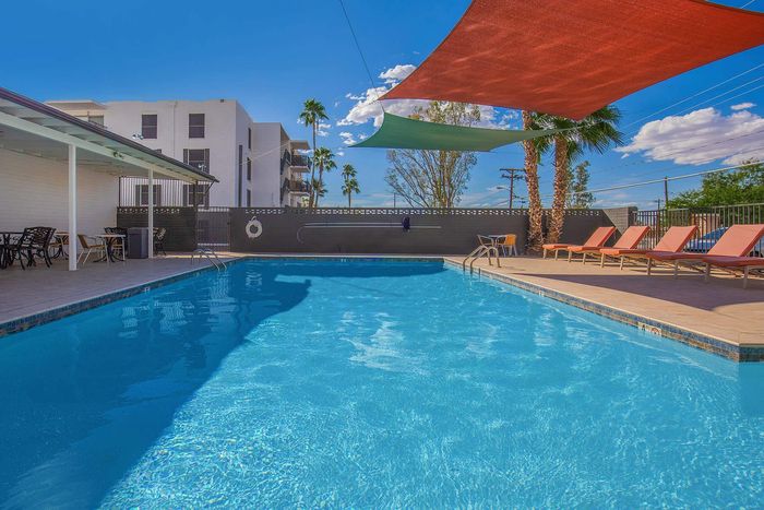 Inviting outdoor pool area with comfortable lounge chairs and vibrant sun sails, perfect for relaxation under the blue sky.
