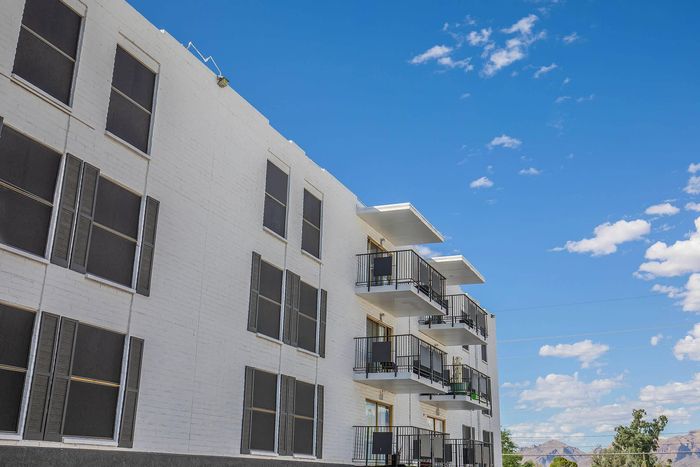 Charming apartment building with white brick facade and sleek balconies set against a vibrant blue sky.