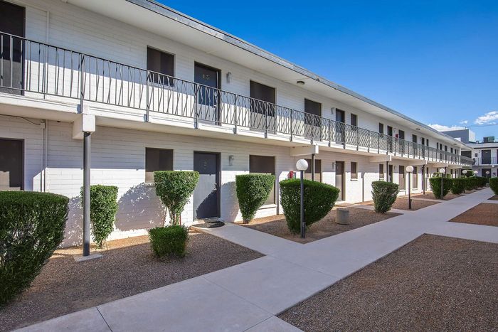 Charming two-story apartment building with modern black doors, lush greenery, and a bright, inviting atmosphere.