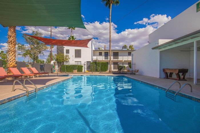 Inviting outdoor pool area with vibrant sun loungers and shaded canopies, perfect for relaxation under the clear blue sky.