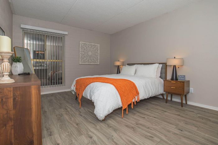 Chic bedroom with modern decor, featuring a cozy bed adorned with crisp white linens and a vibrant orange throw, complemented by stylish wooden furniture and soft lighting.