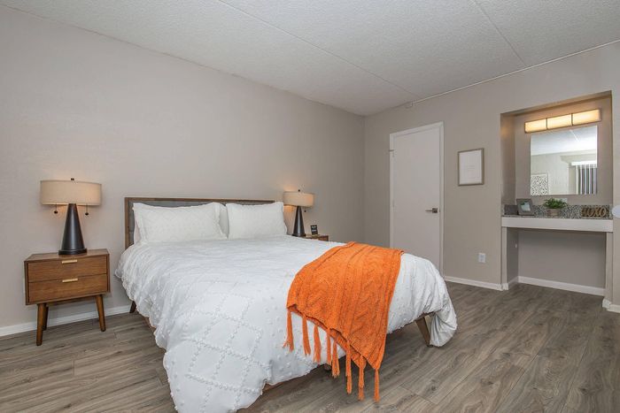 Cozy bedroom with elegant modern decor, featuring a plush bed with a vibrant orange throw, stylish nightstand lamps, and sleek wood flooring.