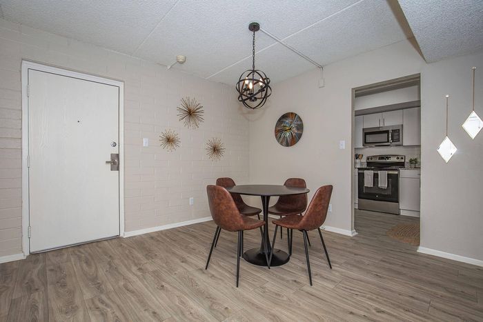 Chic dining area featuring a modern round table with four stylish chairs, set against a textured brick wall adorned with unique metallic art pieces. Nearby, an elegant kitchen with state-of-the-art stainless steel appliances adds sophistication.