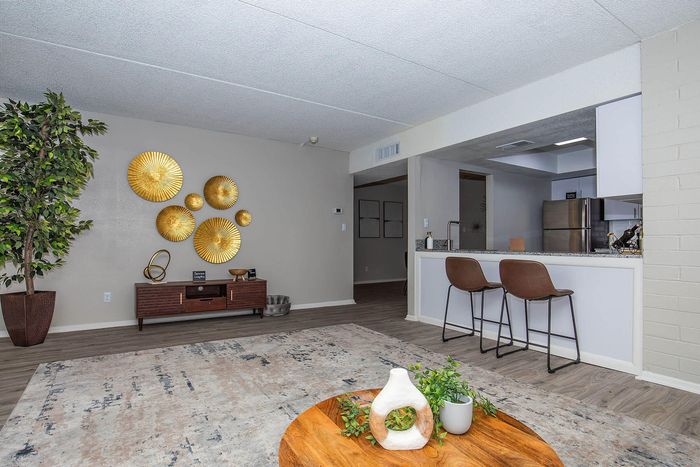 Contemporary living room with sleek bar stools at a granite-top kitchen counter, modern decor, and a stylish potted plant adding a touch of nature.