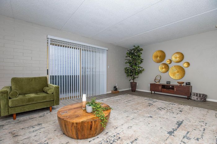 Inviting living room with chic decor, featuring a plush green chair, modern wooden coffee table, and elegant golden wall accents.