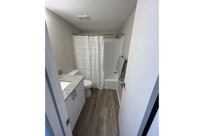 Modern bathroom with elegant granite countertop, sleek cabinetry, and a cozy bathtub-shower combo accented by stylish wood-look flooring.