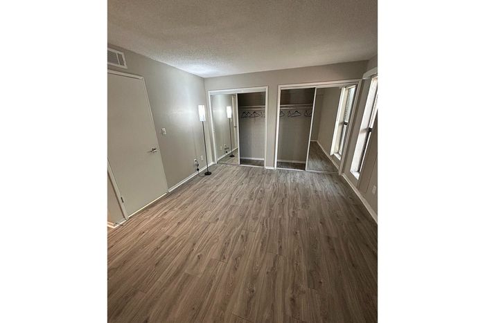 Bright, inviting bedroom with modern wood flooring and spacious mirrored closets.