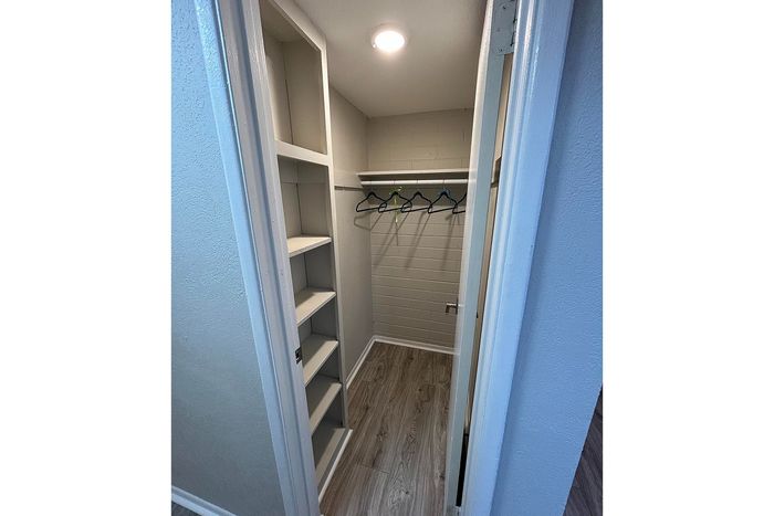 Modern walk-in closet with sleek built-in shelving and wood flooring, featuring ample space for storage and organization.