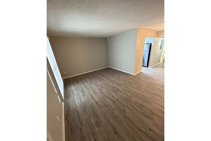 Inviting apartment space with elegant wood-style flooring and abundant natural light, leading to a modern kitchen area.