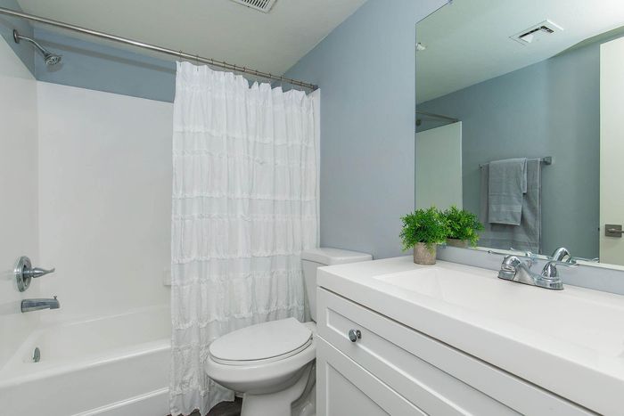 Bright and elegant bathroom with modern fixtures, featuring a chic vanity mirror, white cabinetry, and a fresh green plant accent.