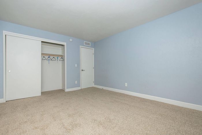 Bright and inviting bedroom with plush carpet, ample closet space, and soothing blue walls.