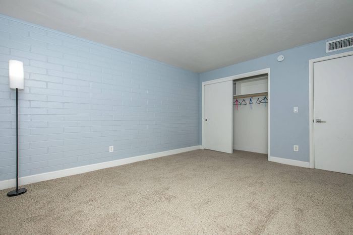 Modern bedroom with soft blue walls, spacious closet, and plush carpeting, offering a serene and open space perfect for relaxation.