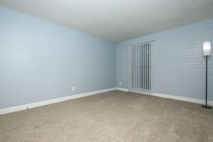 Inviting empty room with soft gray walls, plush carpeting, large window with vertical blinds, and modern floor lamp.