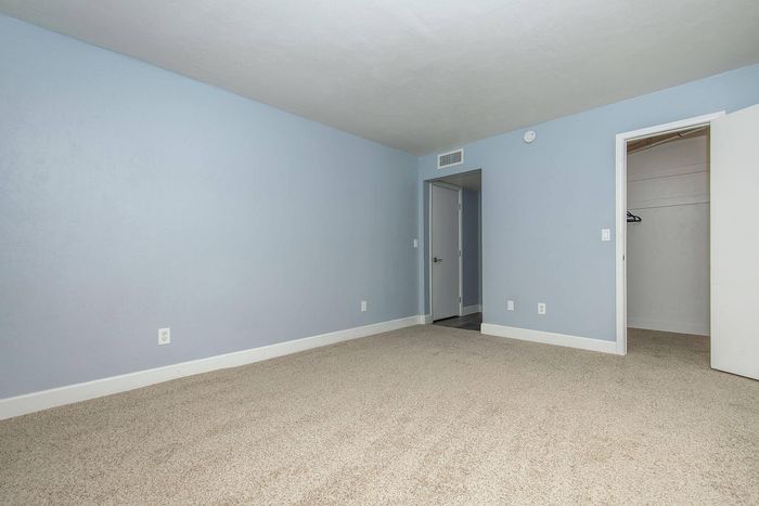 Spacious bedroom with soothing light blue walls, plush carpet, and ample closet space in a modern apartment.