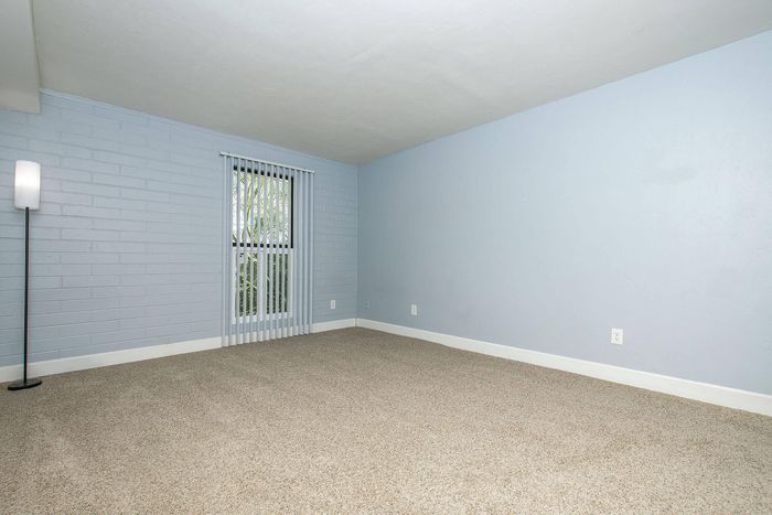 Bright and airy empty room with soft carpeting, stylish light blue walls, and vertical blinds filtering natural light, perfect for personalized decor.