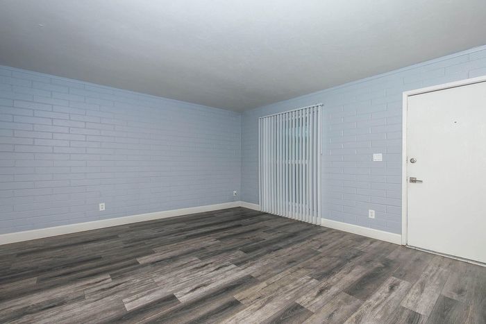 Modern living space featuring sleek wood flooring, light blue painted brick walls, and vertical blinds creating a bright and inviting atmosphere.