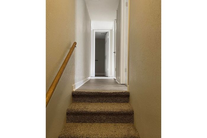 Inviting carpeted staircase leading to a bright, modern hallway with natural light pouring through, highlighting the sleek design.