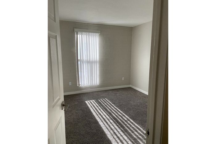 Inviting bedroom with soft carpeting, warm natural light, and modern vertical blinds.
