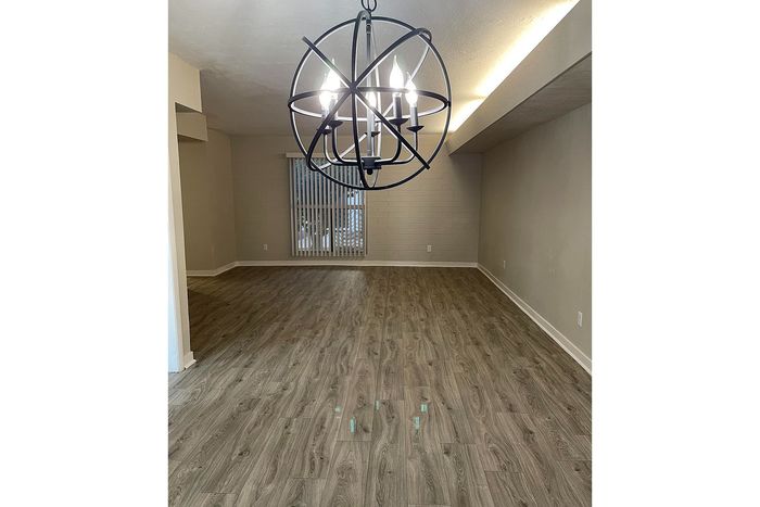 Modern living space with elegant chandelier lighting, stylish wood flooring, and large window with vertical blinds.