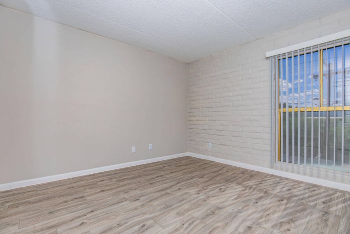 Spacious empty room with elegant wood flooring, large window with vertical blinds, and a soft neutral color palette.