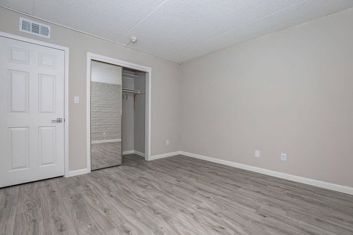 Chic and modern bedroom with elegant wood flooring and a spacious closet featuring mirrored sliding doors.