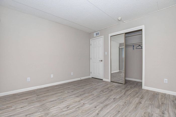 Spacious and modern bedroom with sleek wooden flooring, a large mirrored closet door, and neutral walls, offering a blank canvas for personalized style.
