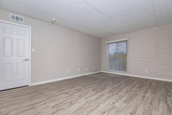 Bright, modern living space with elegant wood flooring and large window featuring vertical blinds, perfect for seamless indoor-outdoor flow.