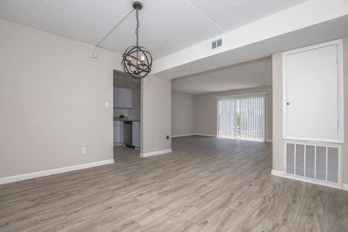 Bright open living space with modern wood flooring, adjacent kitchen, and large sliding glass doors for natural light.