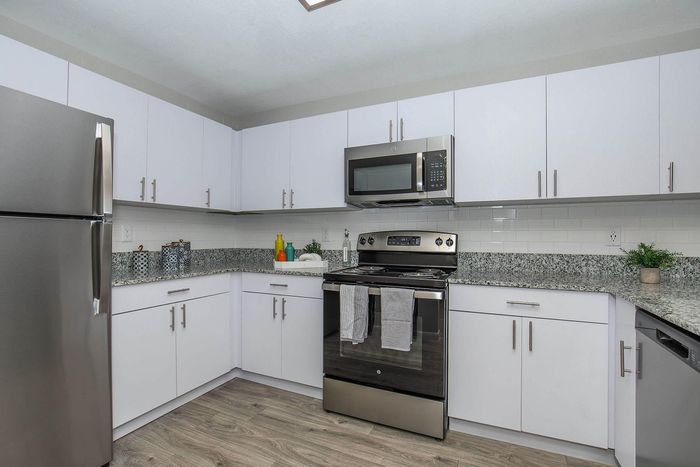 Modern kitchen with sleek stainless steel appliances, white cabinetry, and granite countertops featuring a stylish backsplash.