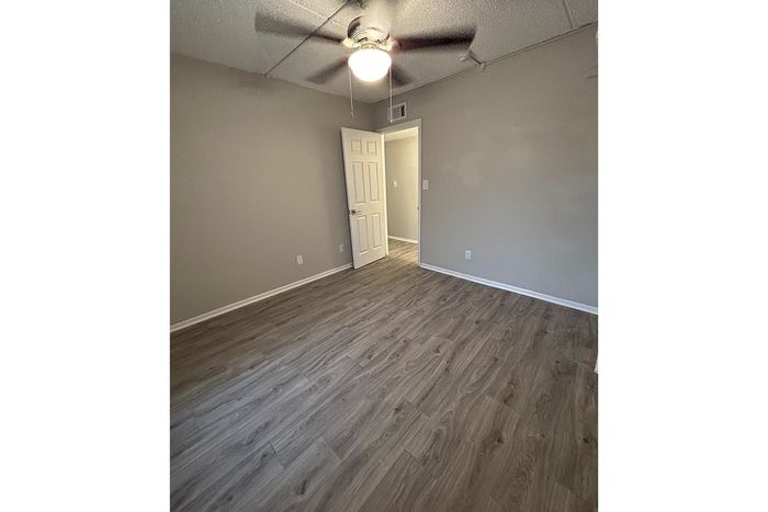 Inviting bedroom with elegant wood flooring, a sleek ceiling fan, and neutral walls offering a modern, serene ambiance.