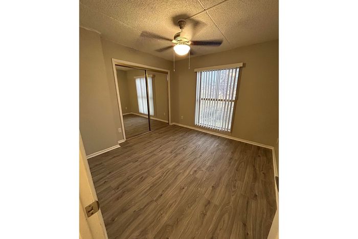 Bright and inviting bedroom with elegant wooden flooring, large mirrored closet, and abundant natural light.