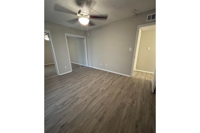 Spacious bedroom with elegant wood flooring, mirrored closet doors, and ceiling fan for a modern living experience.