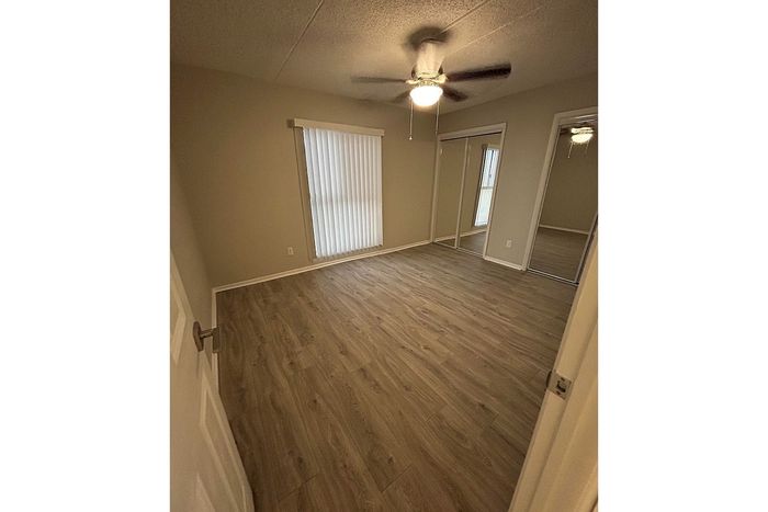 Bright apartment bedroom with elegant wood flooring, ceiling fan, and mirrored closet doors.