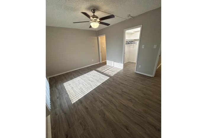 Bright and inviting bedroom featuring elegant wood flooring and a ceiling fan, with ample closet space for a comfortable living experience.