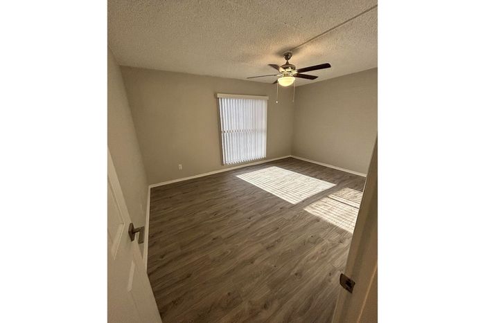 Bright and airy room with modern wood flooring, ceiling fan, and natural light streaming through large window blinds.