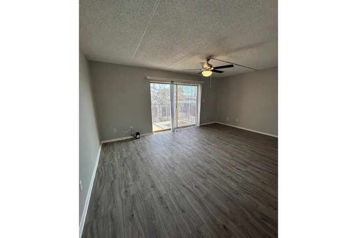 Inviting living room with sleek wood flooring, large window, and modern ceiling fan, offering a bright and airy atmosphere.