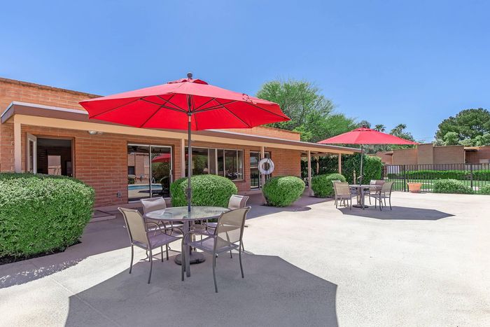 Inviting outdoor patio area with vibrant red umbrellas, elegant seating, and lush greenery, perfect for relaxation and entertaining.