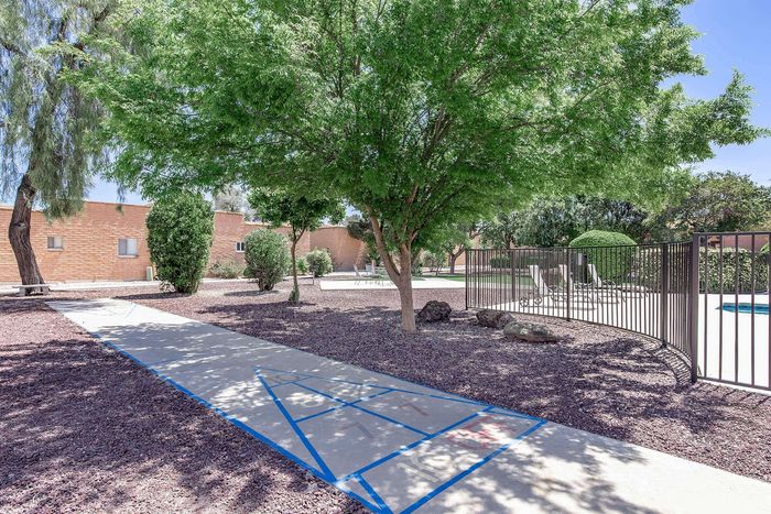 Charming outdoor area featuring a peaceful patio, lush green trees, and a playful shuffleboard court.