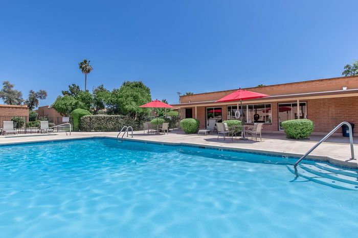 Inviting outdoor pool area with vibrant red umbrellas, lush green landscaping, and a serene blue sky backdrop.