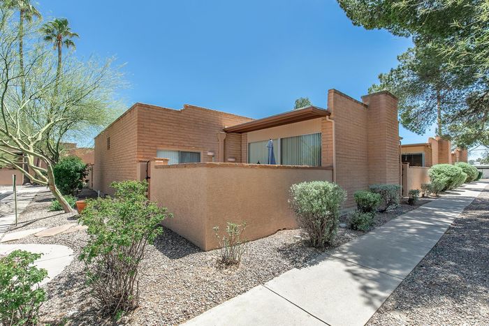 Charming brick apartment with a private patio surrounded by lush landscaping and vibrant desert trees.