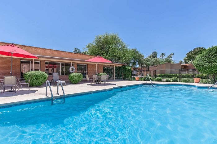 Inviting outdoor pool area with clear blue water, surrounded by stylish patio seating, red umbrellas, and lush greenery.