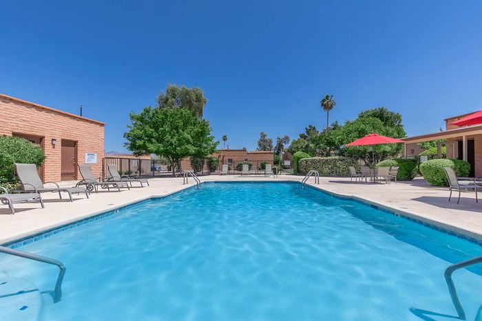 Inviting outdoor pool area with comfortable lounge chairs, vibrant umbrellas, and lush greenery under a clear blue sky.