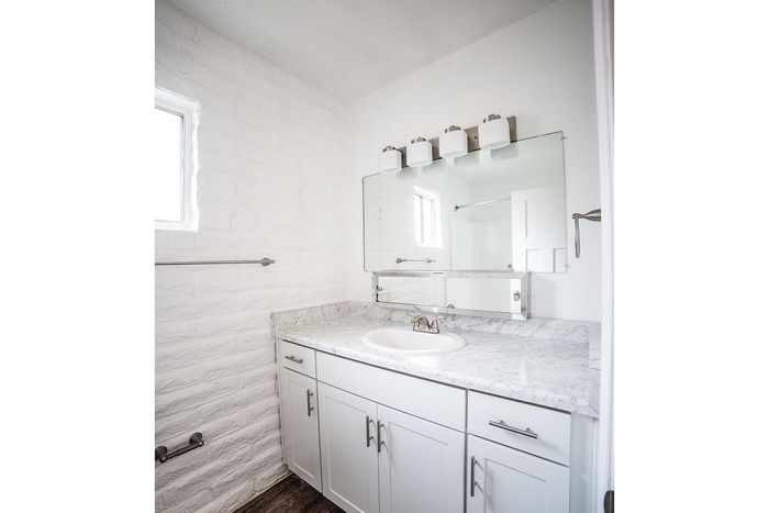 Bright and elegant bathroom with white cabinetry, sleek marble countertop, and modern mirror lighting.
