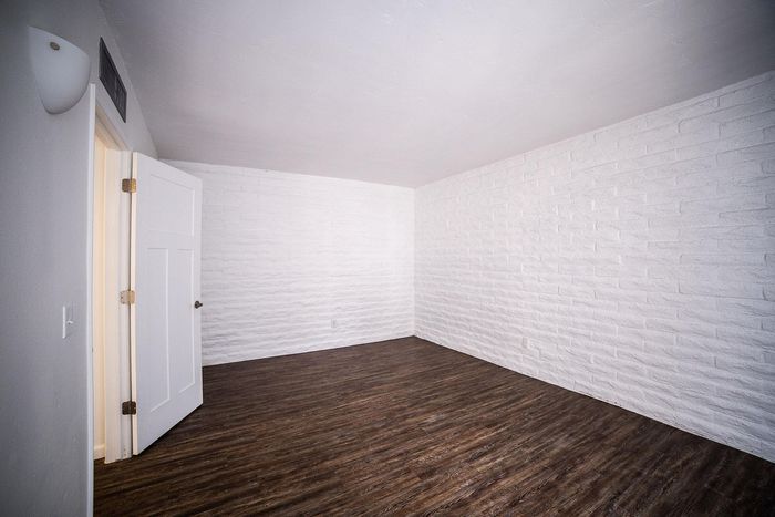 Bright and airy room with textured white brick walls and elegant dark wood flooring, perfect for a modern touch.