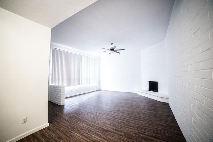 Bright and spacious living area featuring sleek wooden flooring, modern ceiling fan, and large windows with vertical blinds.